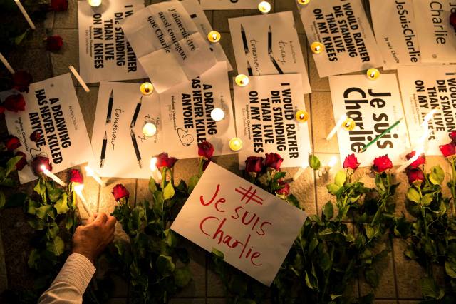 A man places a candle next to messages and flowers during a vigil at the Bangkok Art and Culture Centre to pay tribute to the victims of a shooting by gunmen at the offices of weekly satirical newspaper Charlie Hebdo in Paris